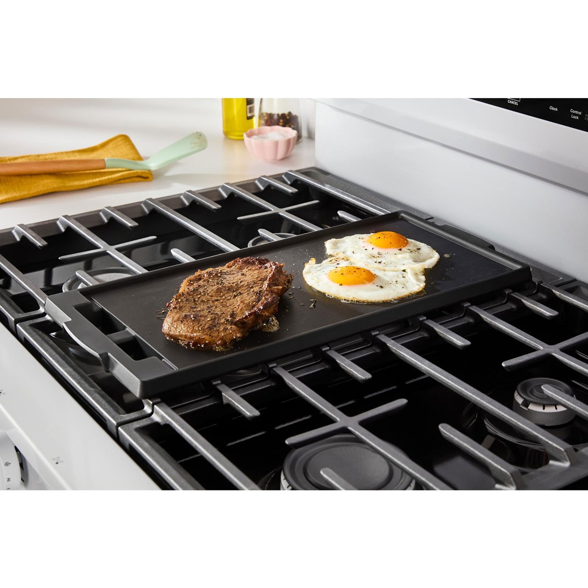 Griddle spanning the center oval burner cooking steak and eggs.