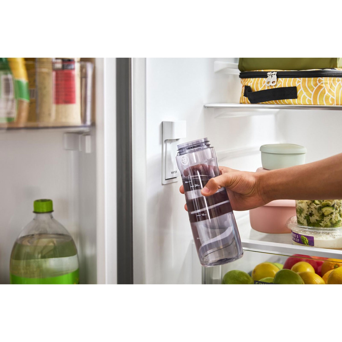 Hand filling a water bottle from the interior filtered water dispenser inside the fridge.