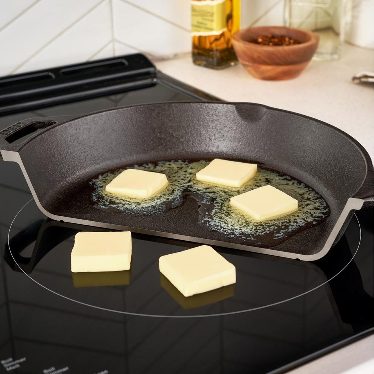 Cast-iron griddle spanning two induction elements melting butter, showing the bridge zone.