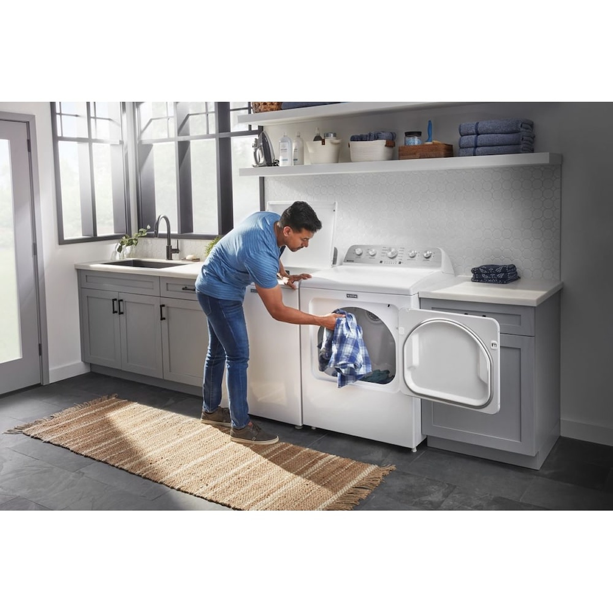 Person loading laundry into a white Maytag dryer in a laundry room