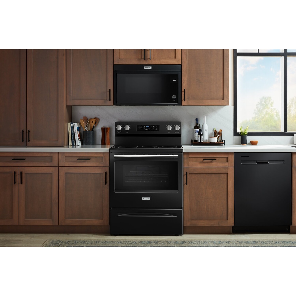 Lifestyle kitchen scene with the black Maytag range installed among wood cabinets and matching appliances.