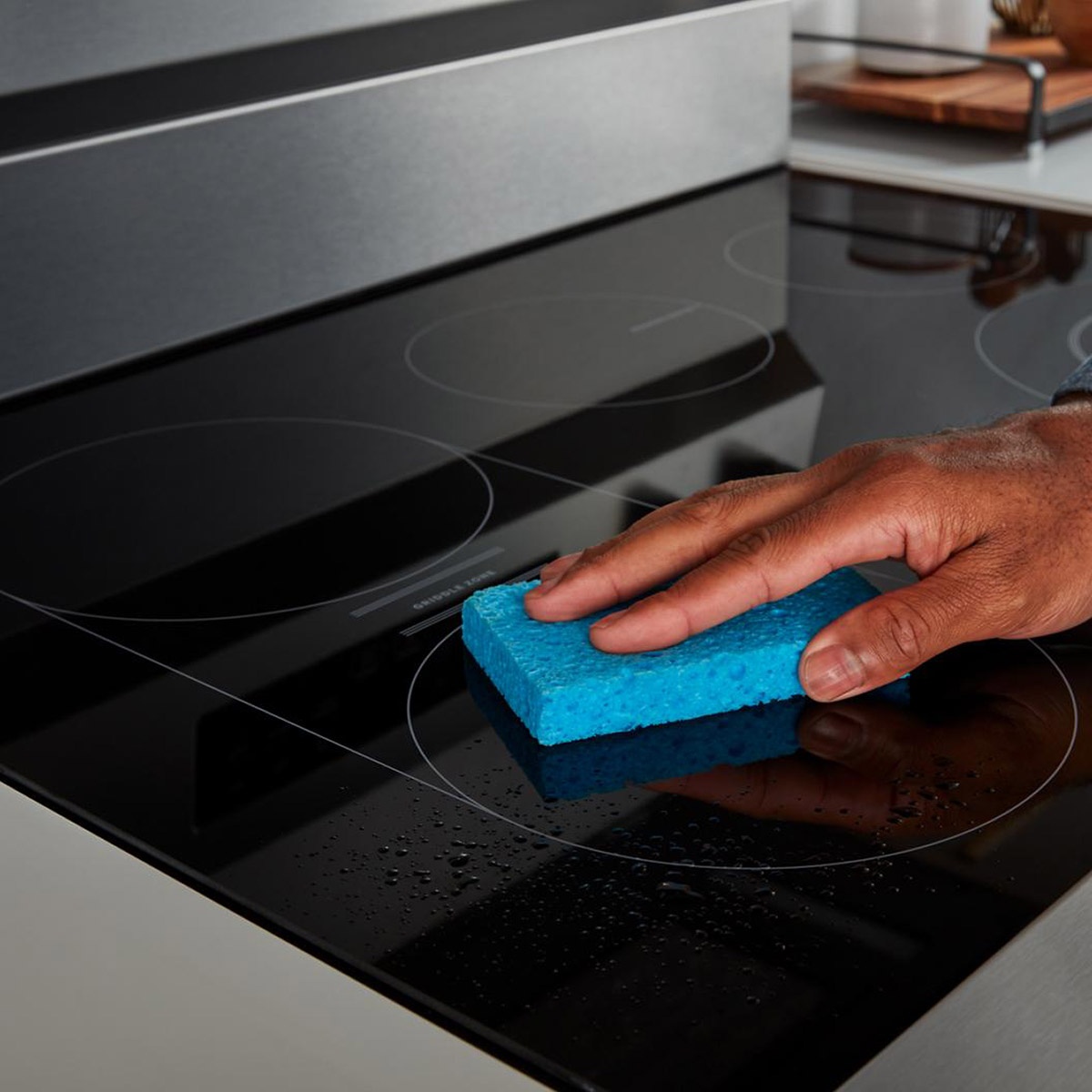 Hand wiping the edge-to-edge glass cooktop with a sponge