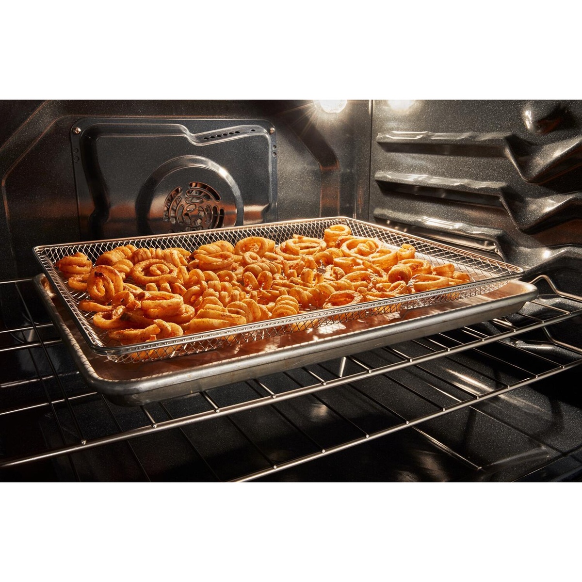 Air fry basket with crispy curly fries inside the oven, fan visible at back