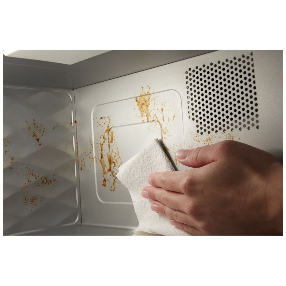 Hand wiping food splatters from the microwave's non-stick interior surface