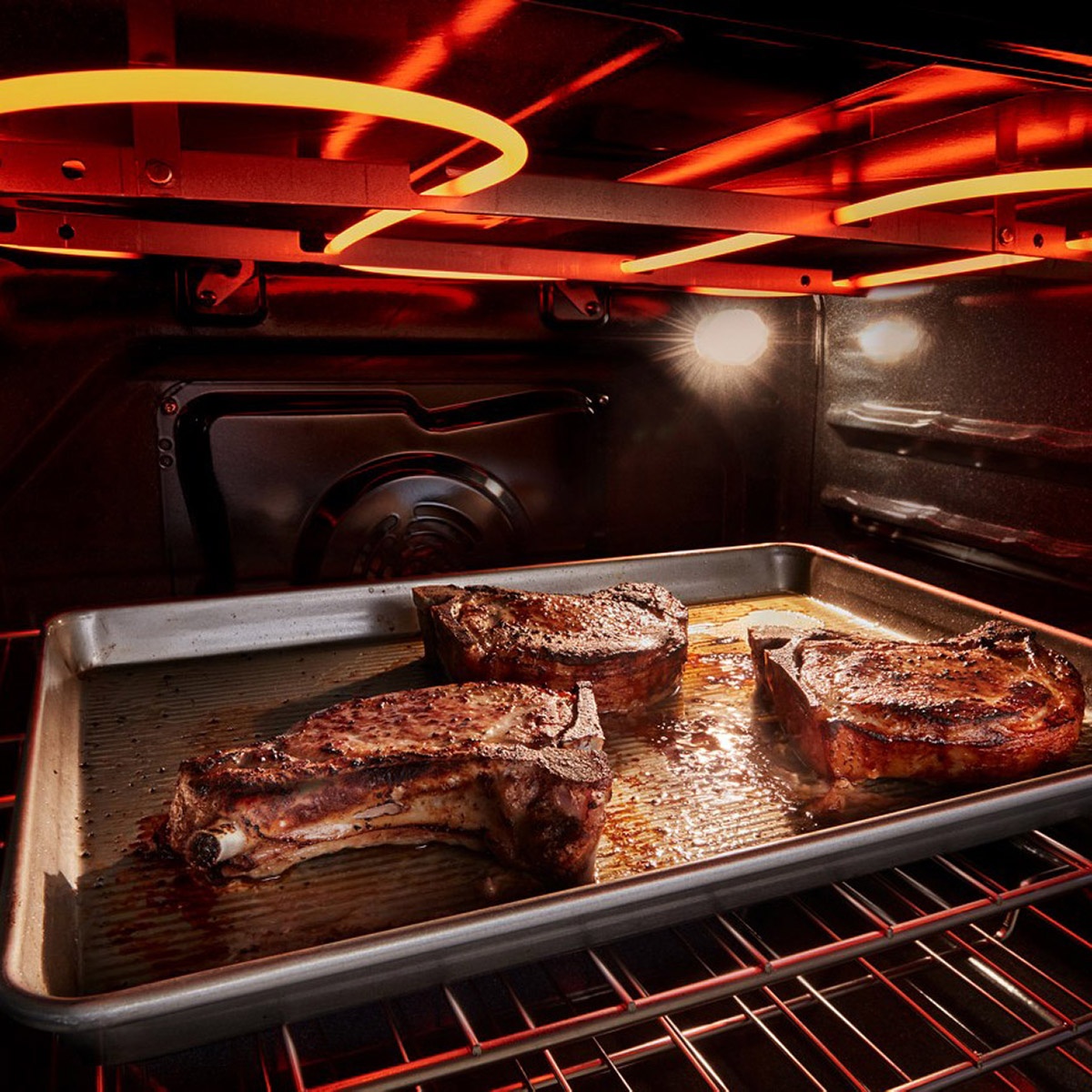Broil element glowing at the top of the oven while searing steaks on a sheet pan