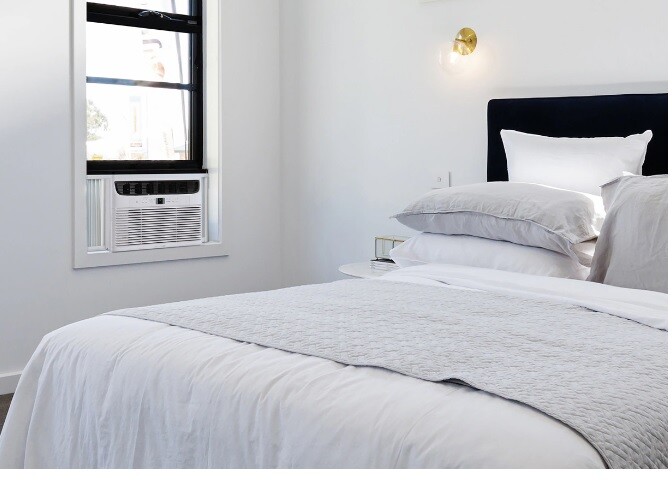 Frigidaire window air conditioner installed in a bedroom window beside a bed