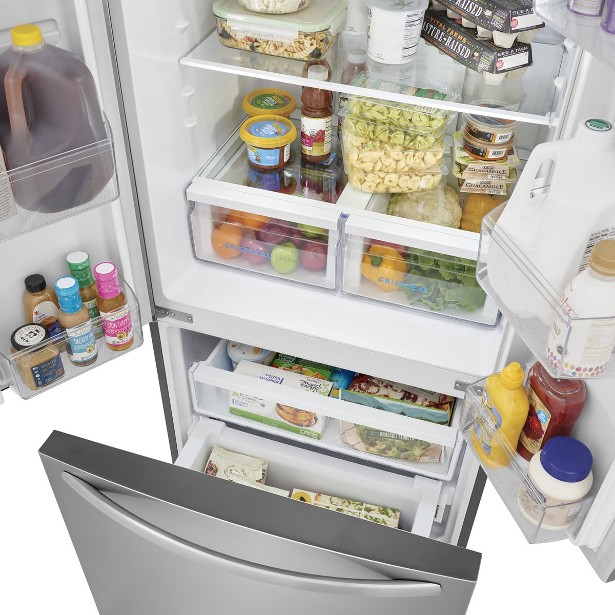 Close-up of the refrigerator interior showing two CrispSeal produce drawers, glass shelving, door bins, and the open bottom freezer drawer