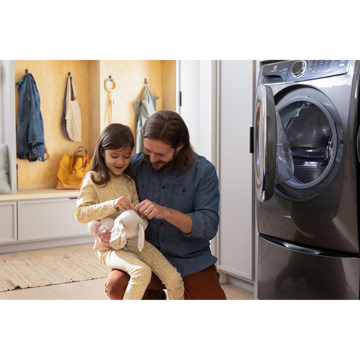 Electrolux front load washer in a mudroom while an adult helps a child, with the washer door open