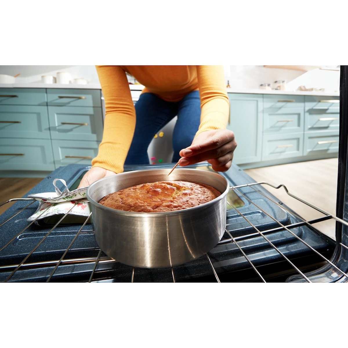 Lifestyle view of a person checking a cake in a pot on the oven rack