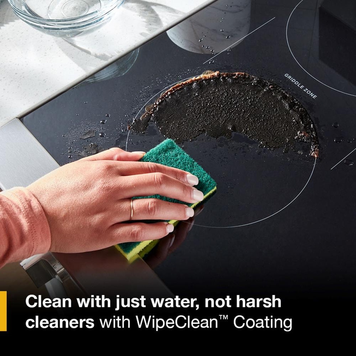 Hand wiping a smooth black cooktop with text about cleaning with just water using WipeClean coating