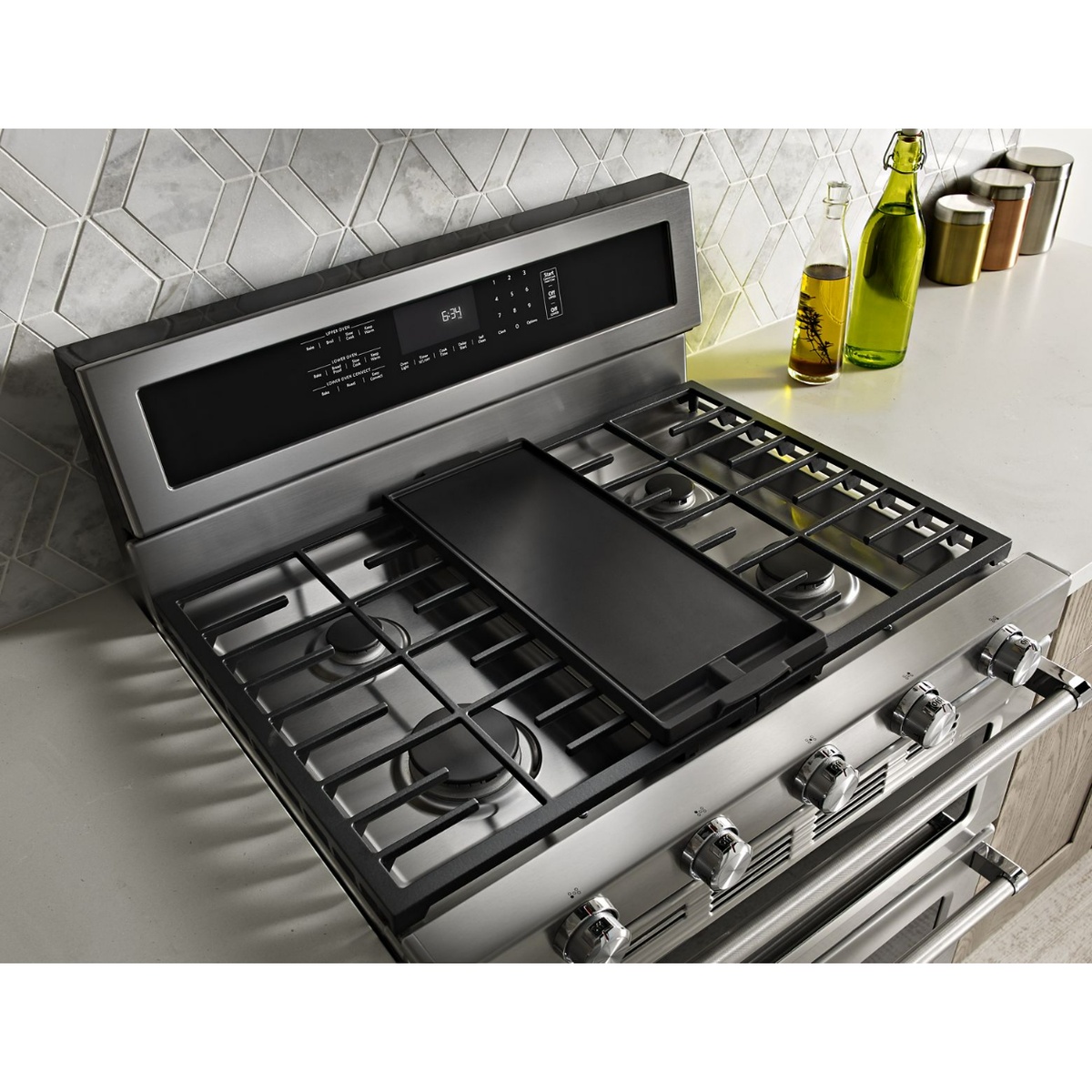 Angled view of the KitchenAid range cooktop with five burner positions, continuous cast-iron grates, and a center griddle shown