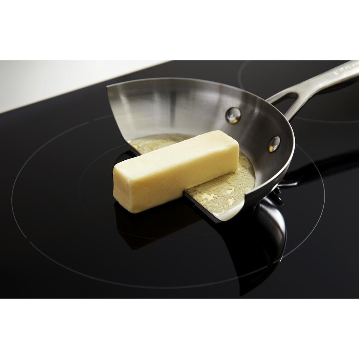 Close-up of a pan melting butter on a smooth black induction cooktop