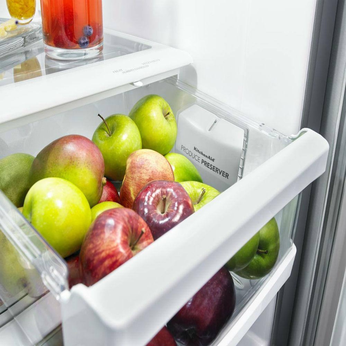 Close-up of a refrigerator crisper drawer filled with apples, with a Produce Preserver cartridge visible inside