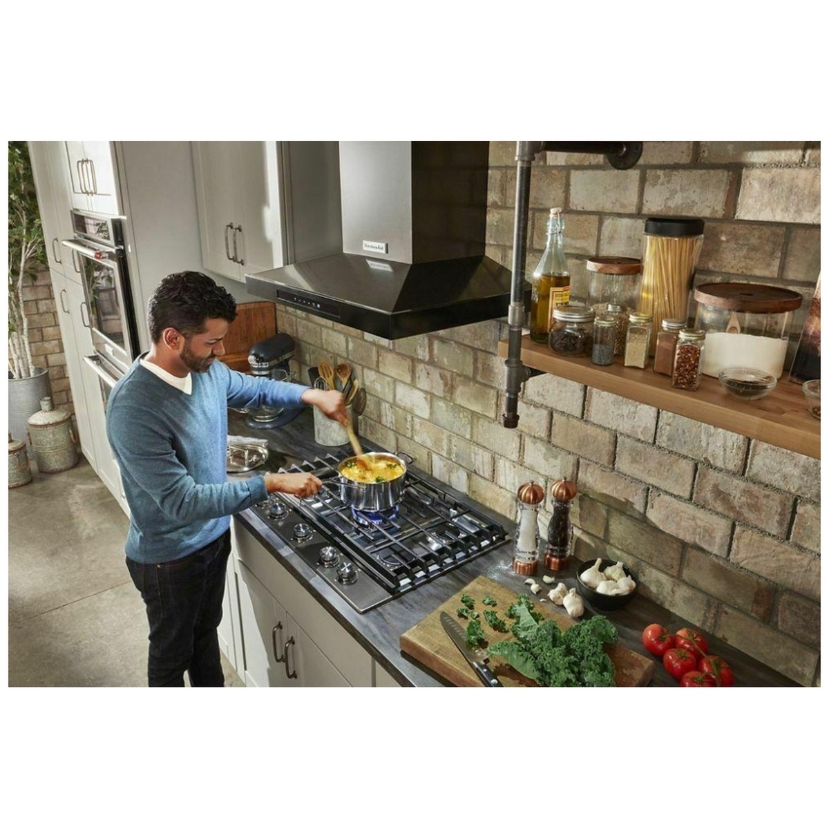KitchenAid wall-mount canopy range hood installed above a cooktop in a kitchen while someone cooks