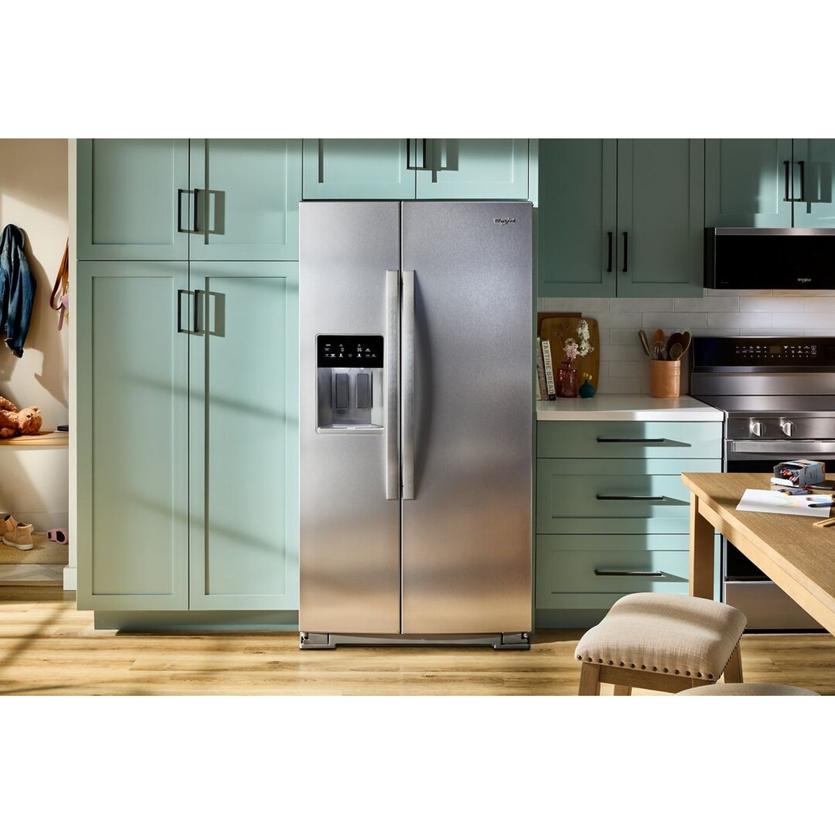 Whirlpool stainless steel side-by-side refrigerator installed in a kitchen with an in-door dispenser