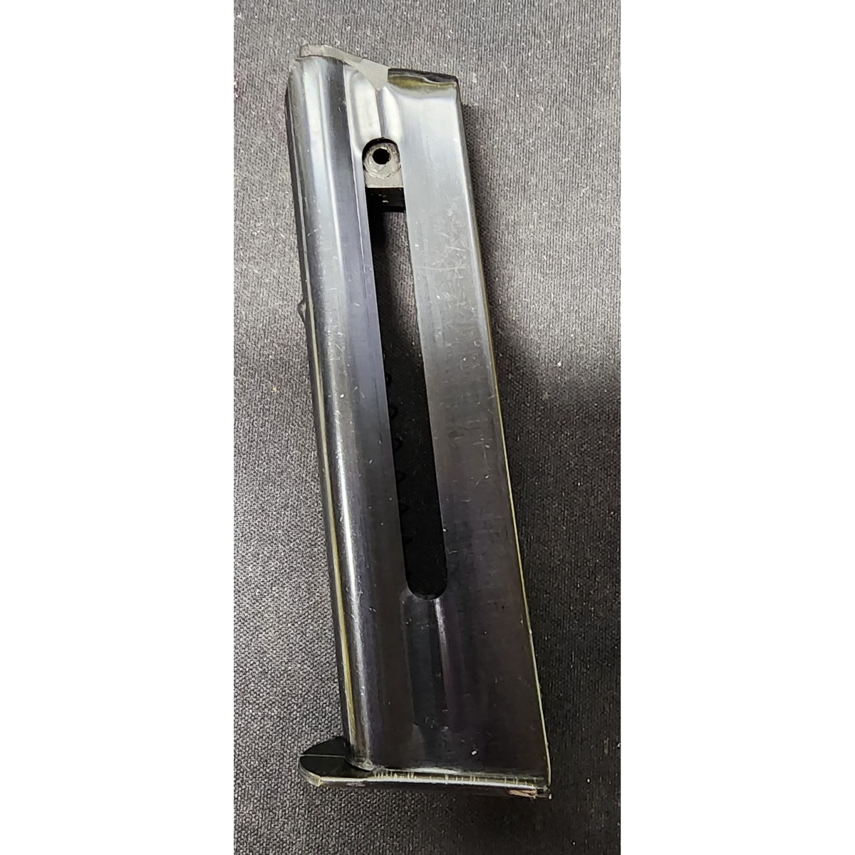 Metal rifle magazine shown from the side on a dark surface