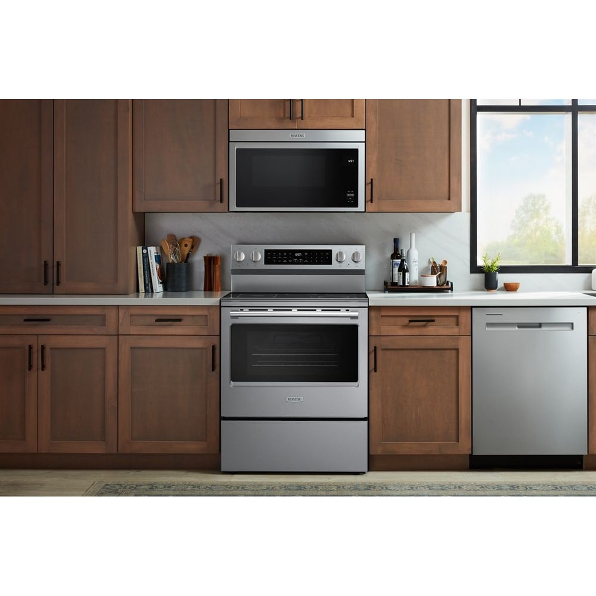 Maytag electric range installed in a kitchen with wood cabinetry, with a matching over-the-range microwave and dishwasher