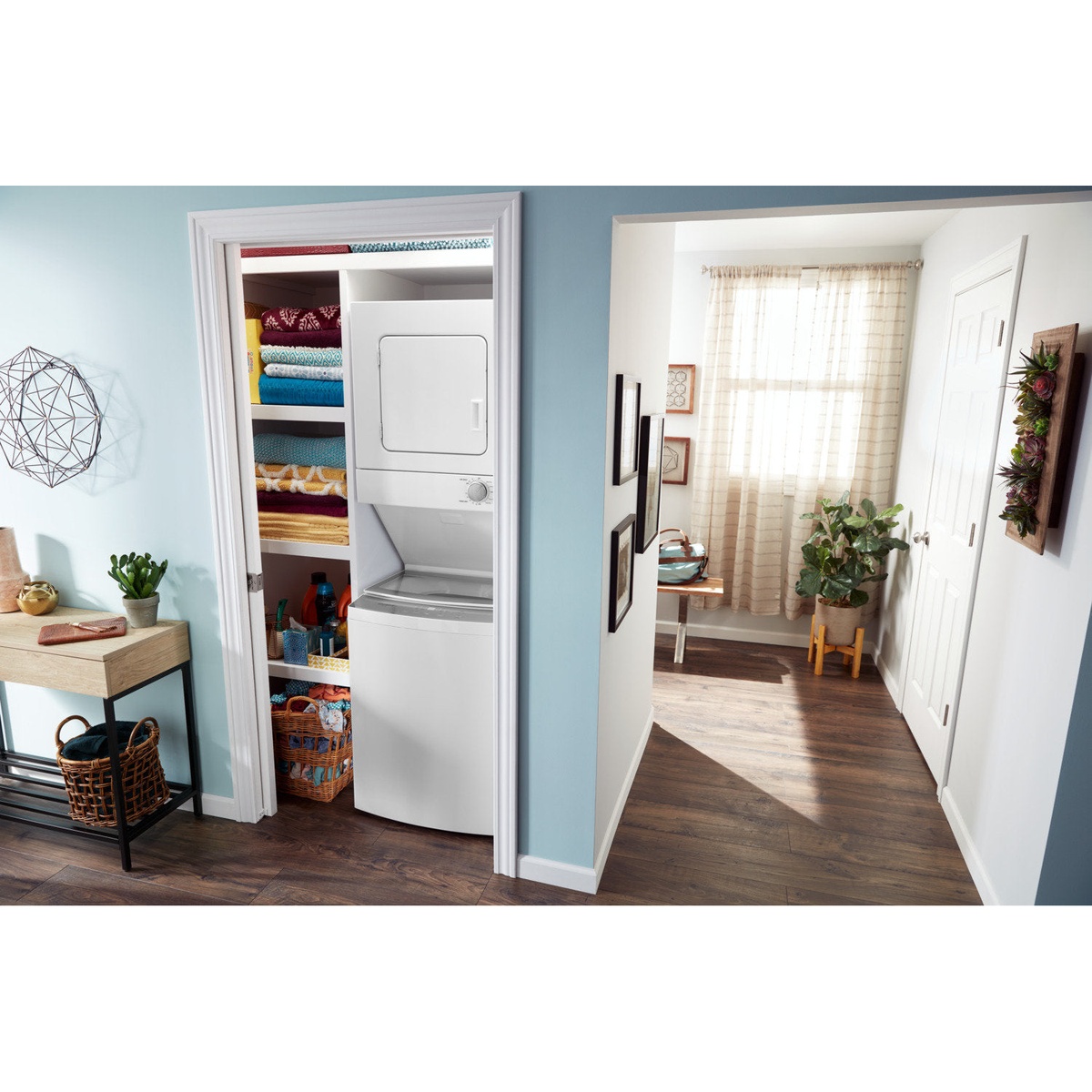 Whirlpool stacked laundry centre installed inside a closet next to shelving with towels and laundry supplies