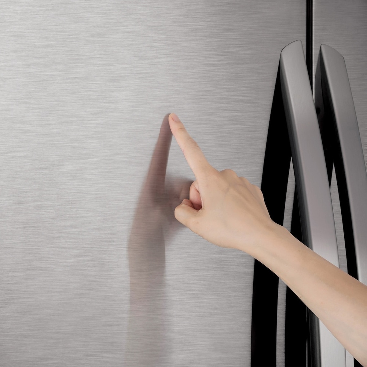 Close-up of a hand touching the stainless steel refrigerator door near the vertical handles