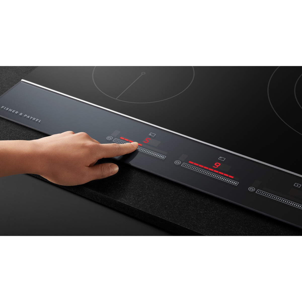 Close-up of the cooktop front edge showing Fisher and Paykel branding and illuminated Touch&Slide controls with a finger adjusting heat level