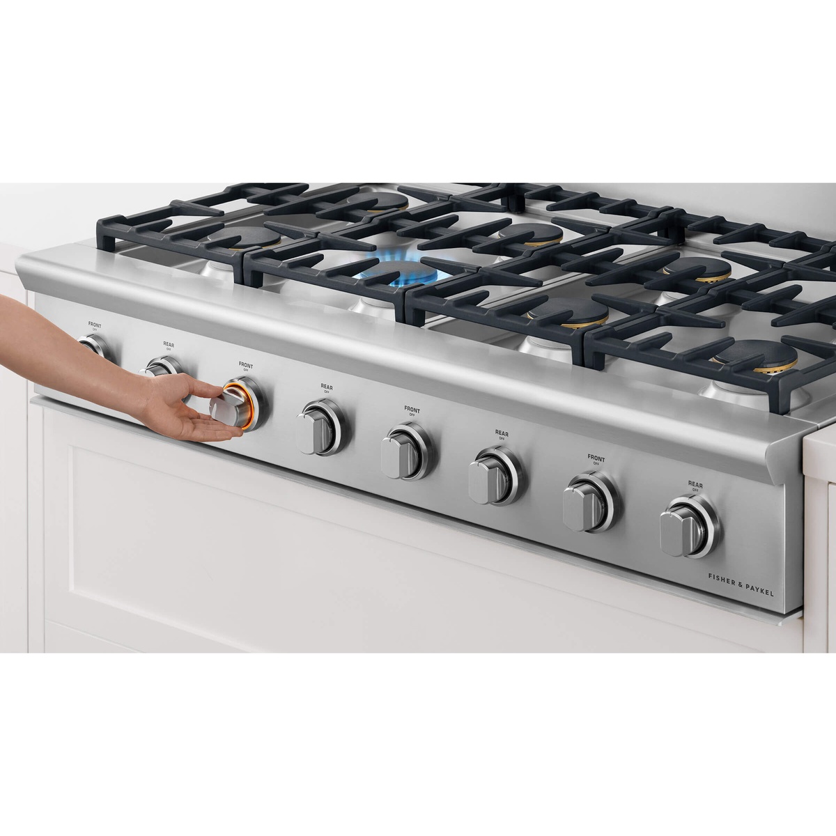 Angled view of a Fisher & Paykel gas rangetop with front control knobs, shown installed in cabinetry with a hand turning a knob