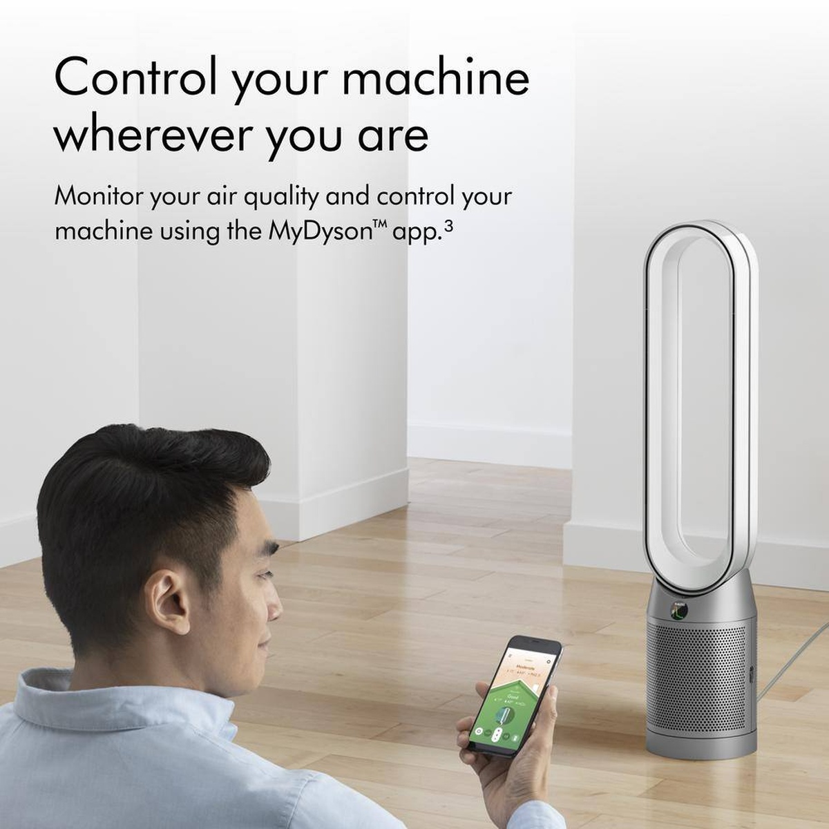 Person holding a smartphone while a Dyson Purifier Cool tower fan sits in a room, with text about controlling the machine with the MyDyson app