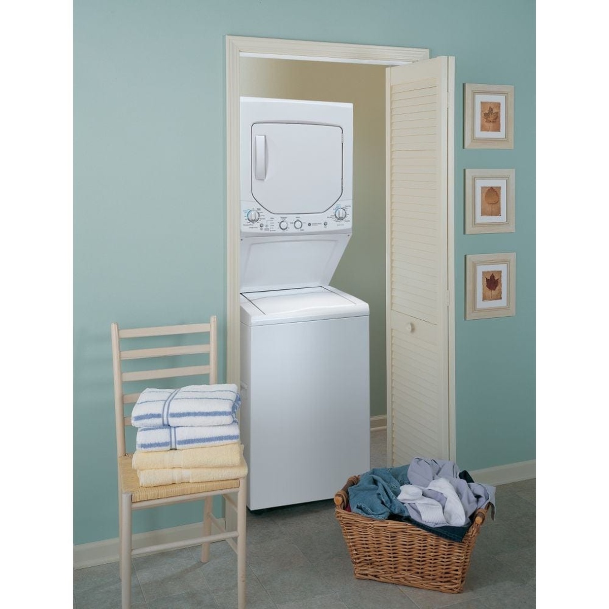 GE stacked washer and dryer laundry centre installed in a small closet beside folded towels and a laundry basket