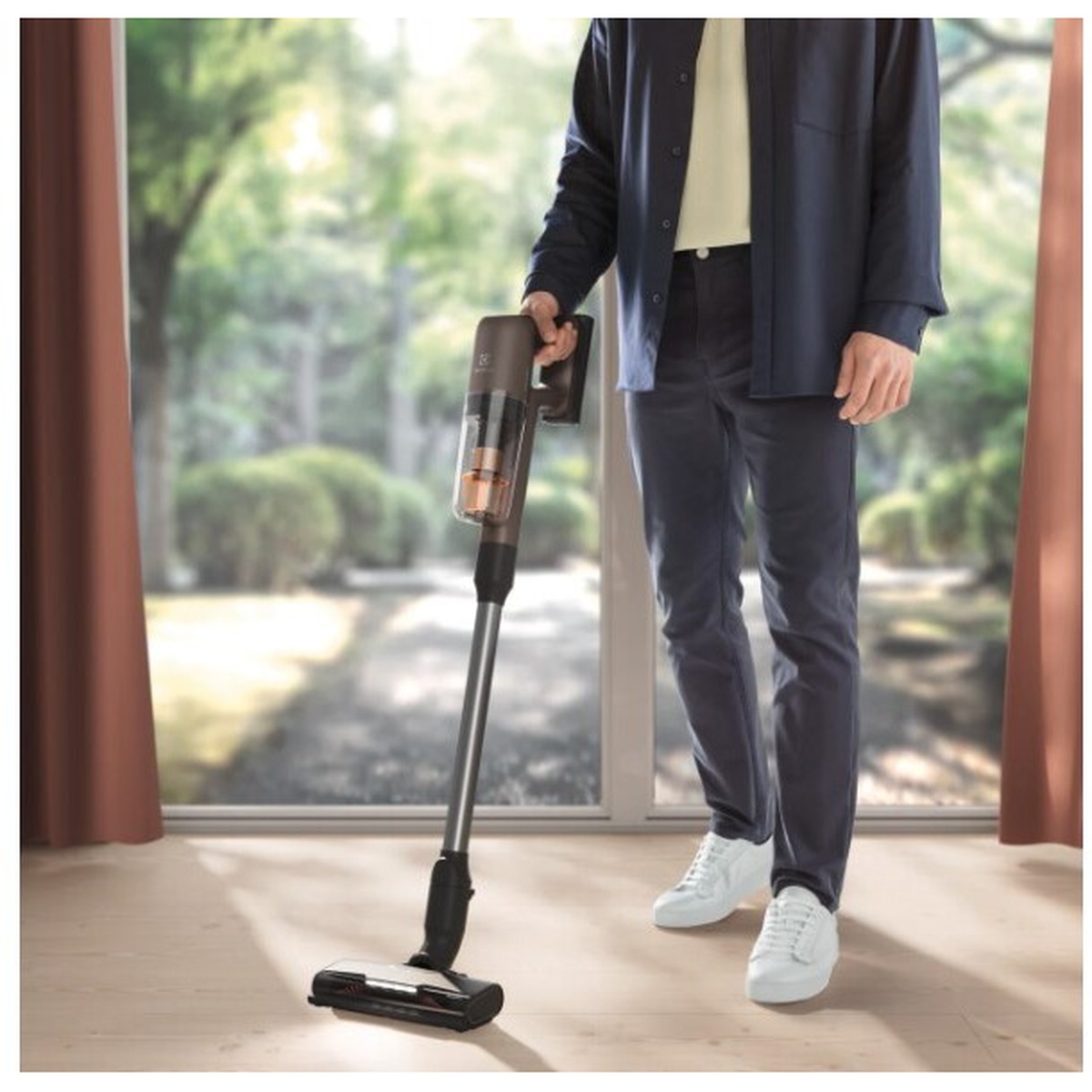 Person using an Electrolux cordless stick vacuum on a hard floor in a bright room