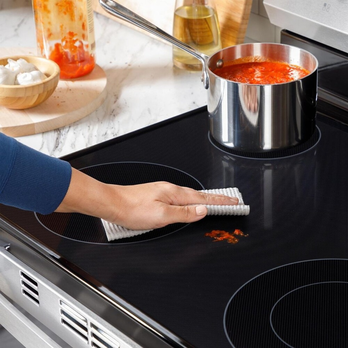 Close-up of a smooth glass cooktop being wiped clean while a pot cooks on another element