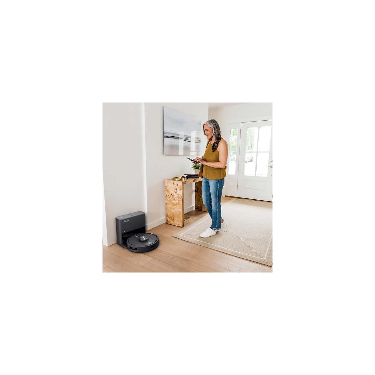 Robot vacuum and base in an entryway while a person controls it with a smartphone