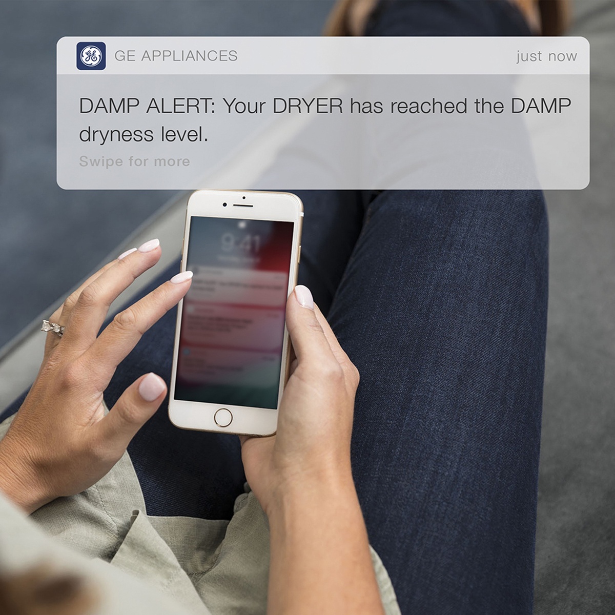 Person holding a smartphone showing a GE Appliances notification that a dryer has reached the damp dryness level.
