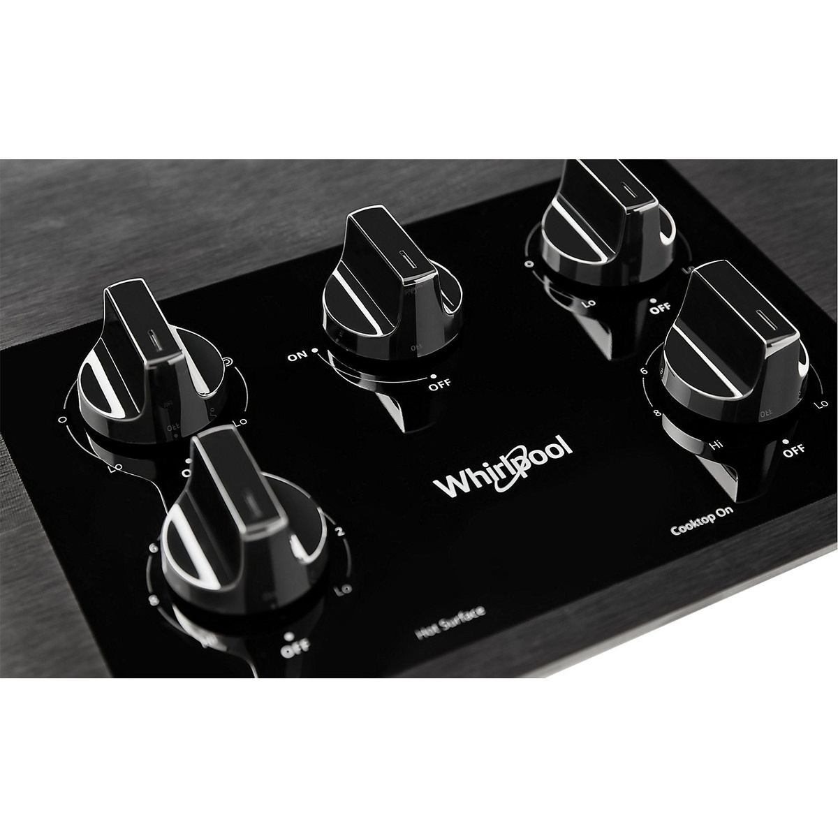 Close-up of the Whirlpool cooktop control area showing four black knob controls on a glossy black glass surface