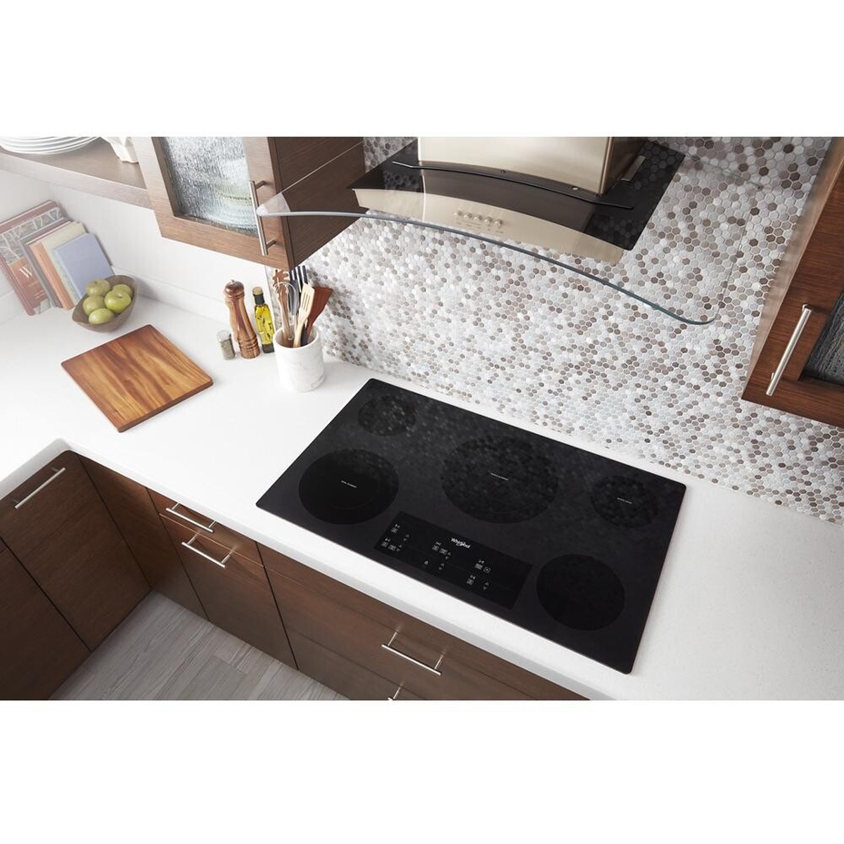 Whirlpool black glass electric cooktop installed flush in a kitchen countertop under a wall hood
