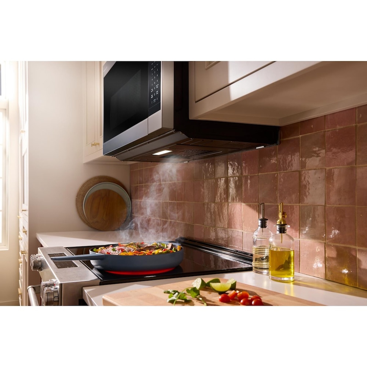 KitchenAid over-the-range microwave installed above a cooktop in a kitchen with steam rising from a pan