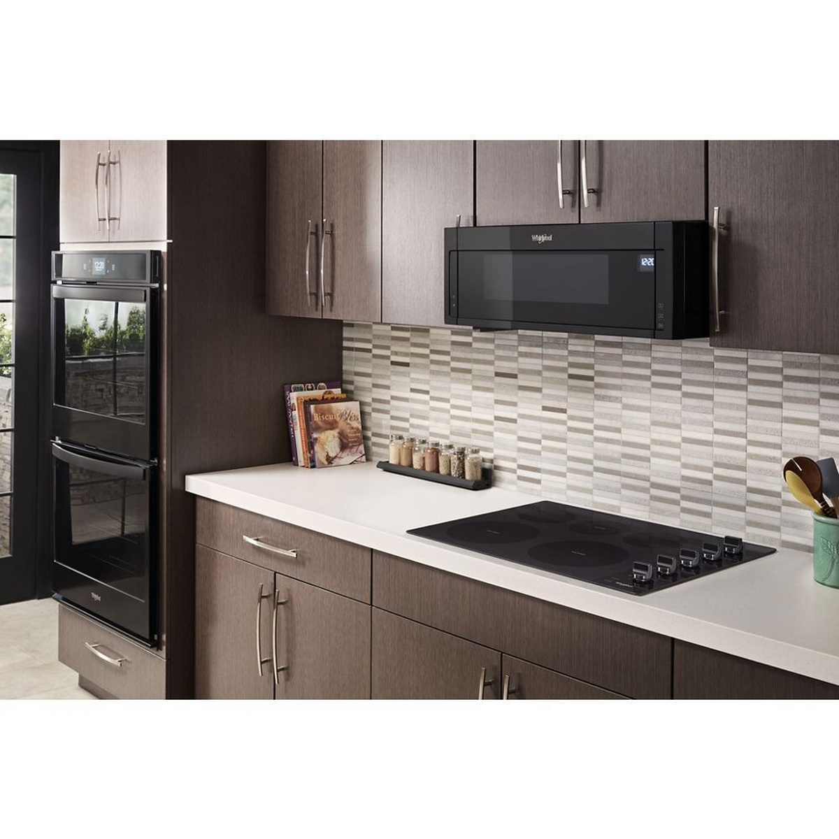 Modern kitchen scene with a black cooktop installed in a countertop, alongside built-in wall ovens and a microwave