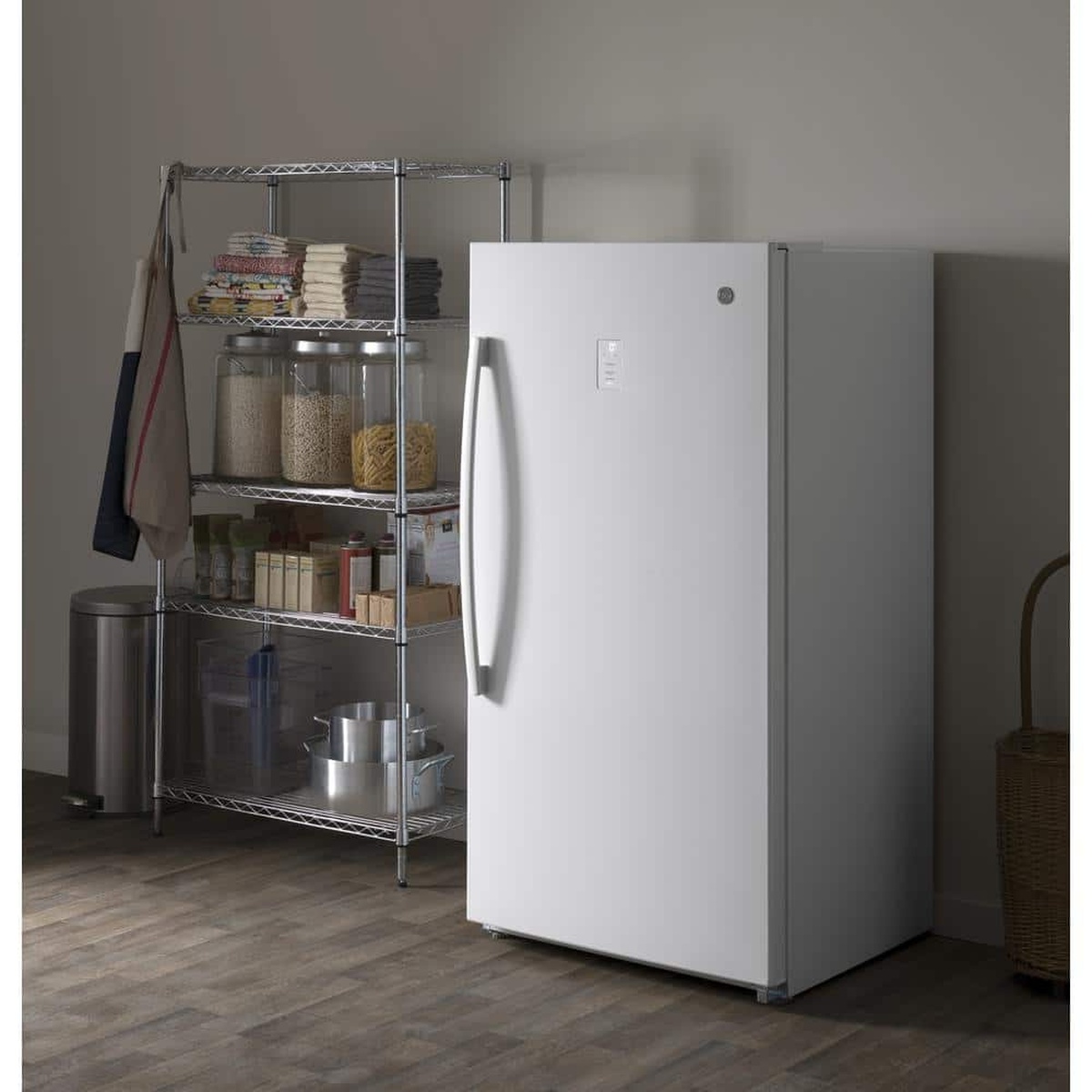 White GE upright freezer in a storage or utility room next to a metal shelving rack