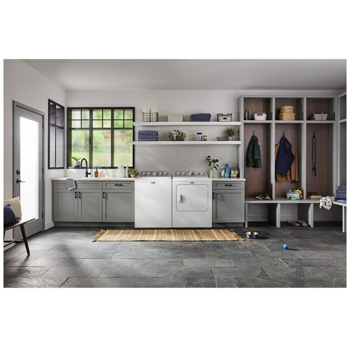 Maytag washer and matching dryer installed side by side in a laundry room with cabinets, shelves, and hanging storage.