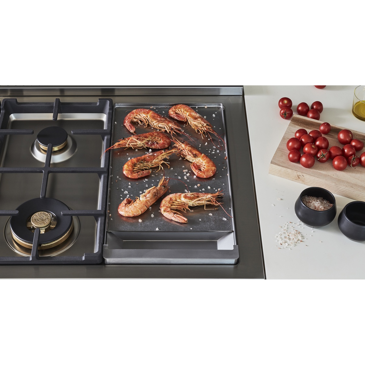 Close-up of the cooktop showing cast iron grates, brass burners, and an integrated griddle with food cooking