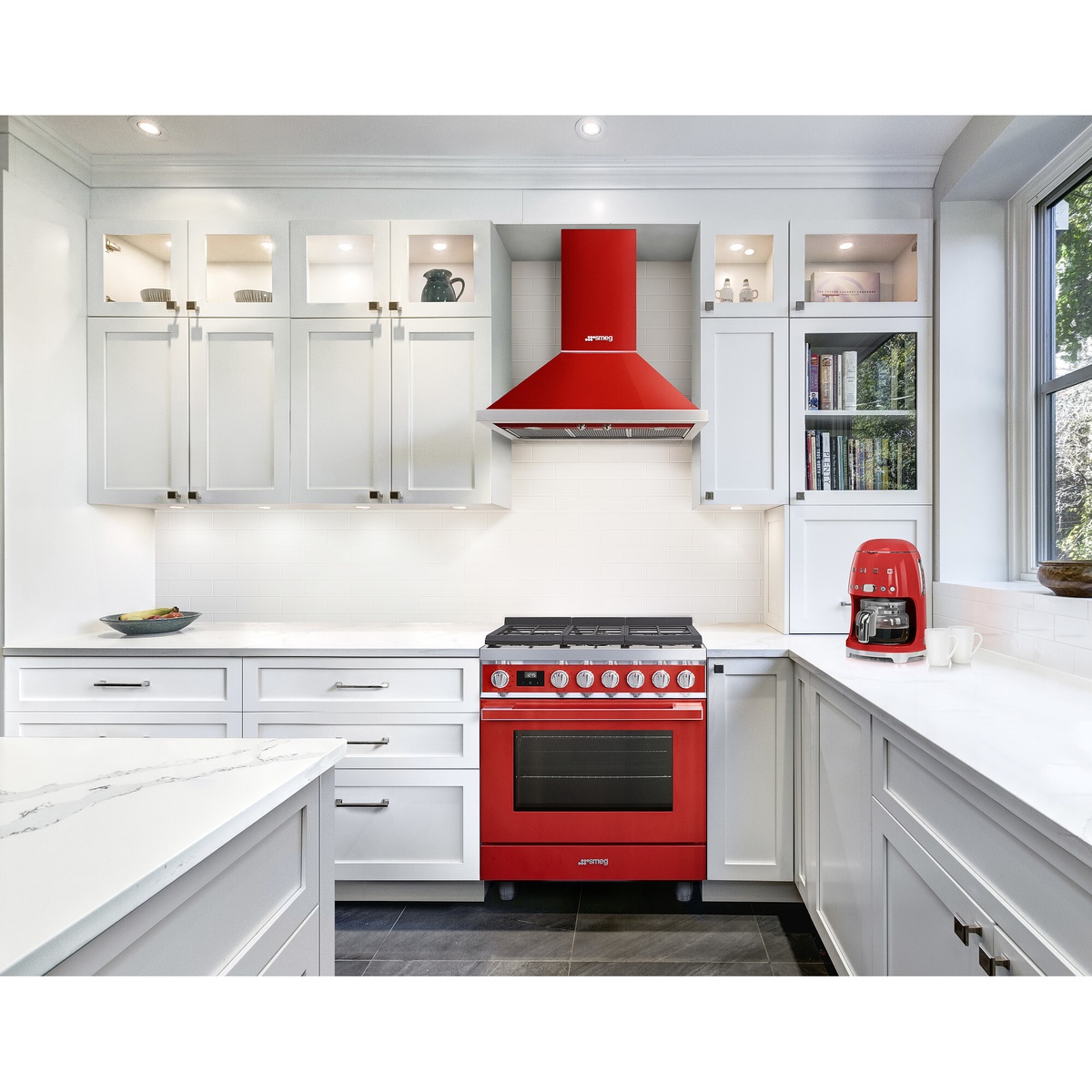 Red Smeg range installed in a bright white kitchen with a matching red range hood and surrounding cabinetry.