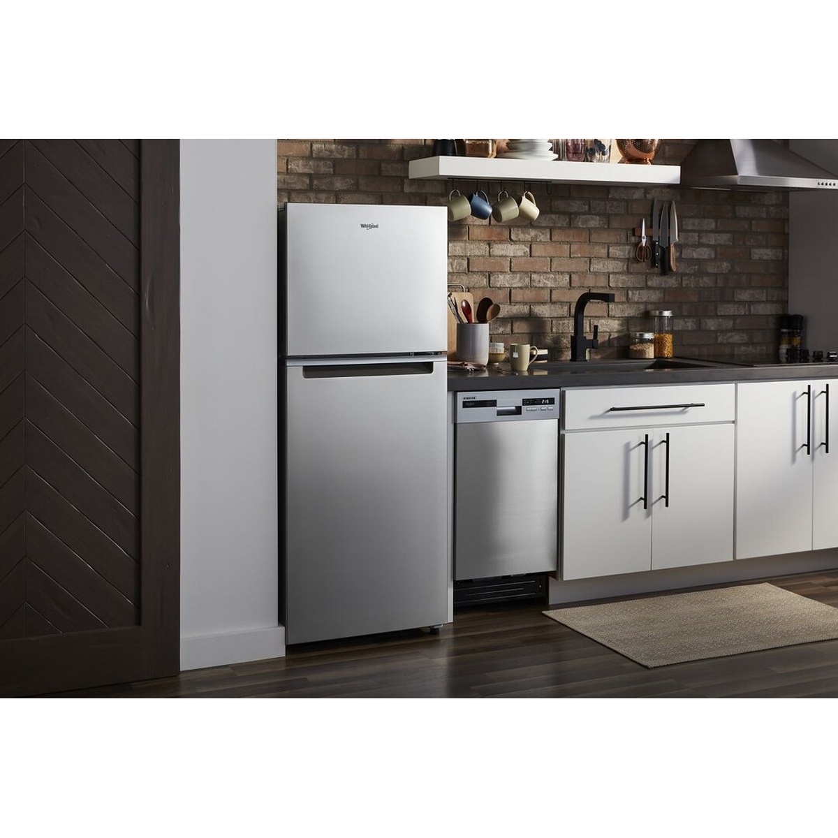 Stainless-look Whirlpool top-freezer refrigerator installed in a compact kitchen next to a dishwasher