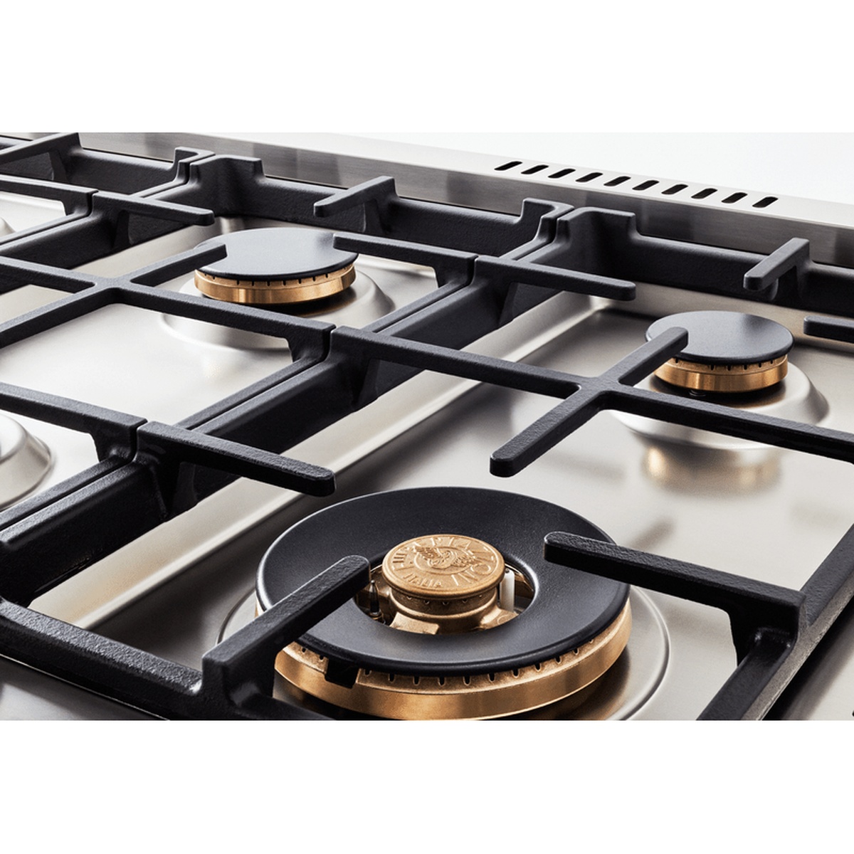 Close-up of brass gas burner caps and continuous cast-iron grates on a stainless steel cooktop