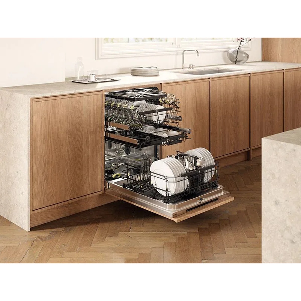 Built-in dishwasher pulled open under a kitchen counter showing three racks loaded with plates, bowls, and glassware.
