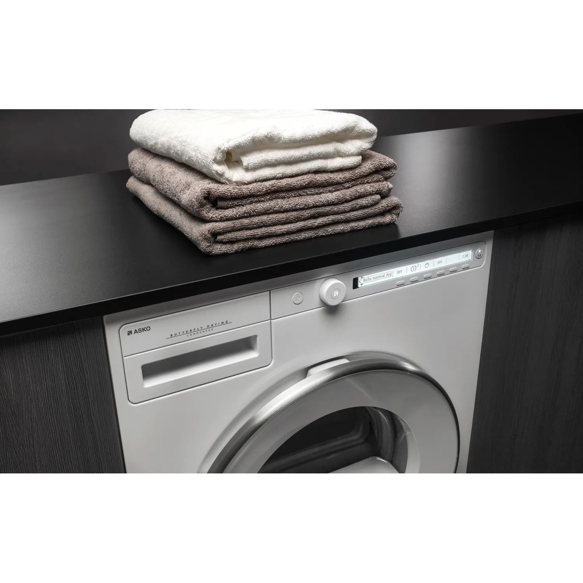 ASKO dryer installed under a countertop with towels on top, showing the control knob and display on the front panel