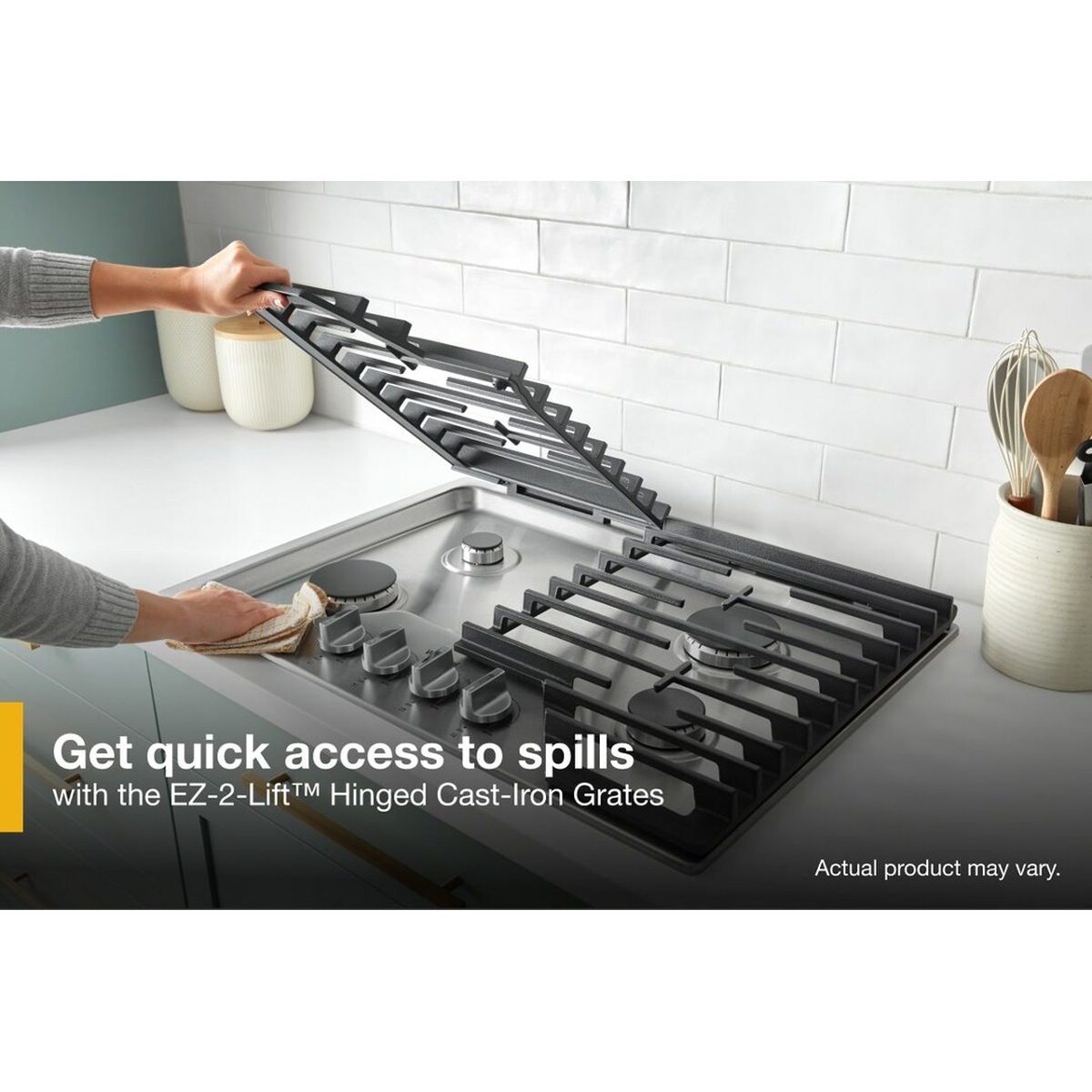 Hand lifting hinged cast-iron grate on Whirlpool gas cooktop to wipe spills from the stainless steel surface below