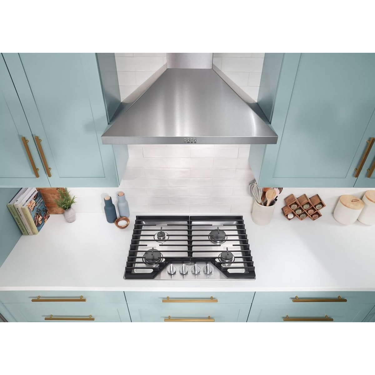 Whirlpool WCGK5030PS gas cooktop installed in a modern kitchen with teal cabinets and a stainless steel range hood, viewed from above
