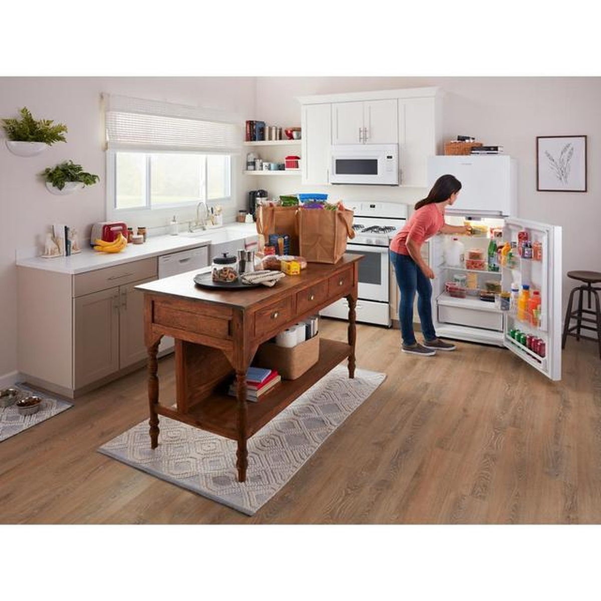 Woman unloading groceries into the open Amana ARTX3028PW top-freezer refrigerator, showing the lit interior, door bins, and shelving