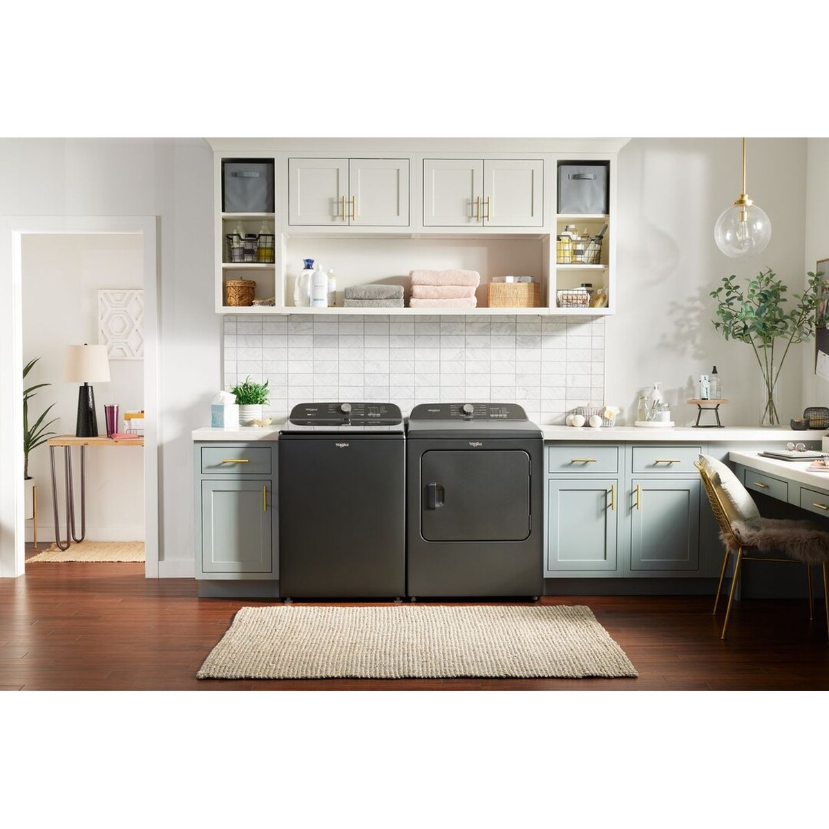 Whirlpool top load washer and dryer pair in Volcano Black set in a bright, styled laundry room with teal cabinetry and open shelving.