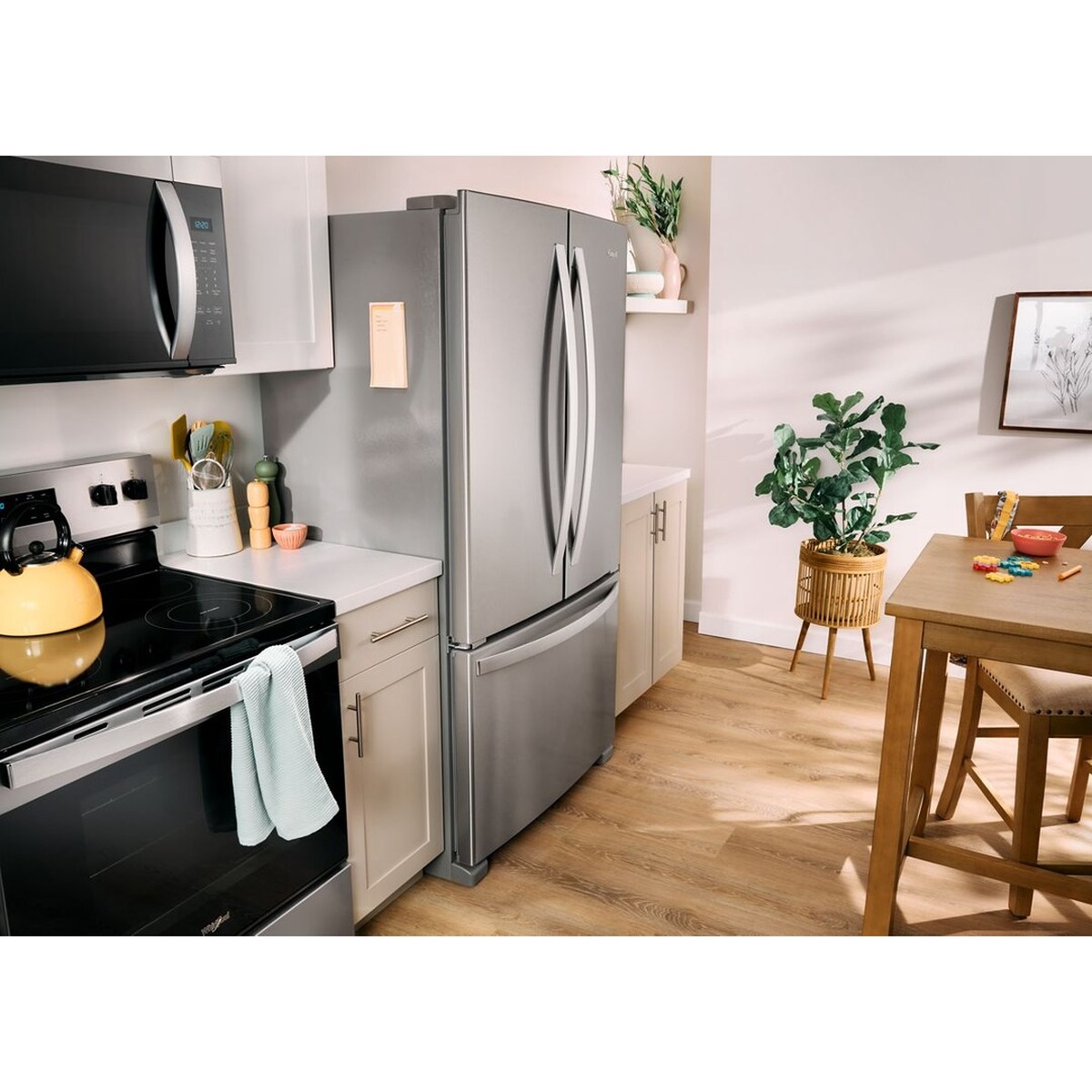 Whirlpool French door refrigerator installed in a bright, modern family kitchen alongside a Whirlpool range and over-the-range microwave, showing the appliances in a lived-in home setting.