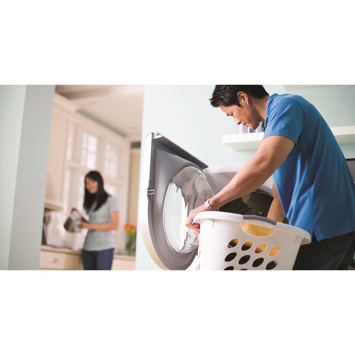 Man loading laundry into a front-load washer from a laundry basket in a bright home setting