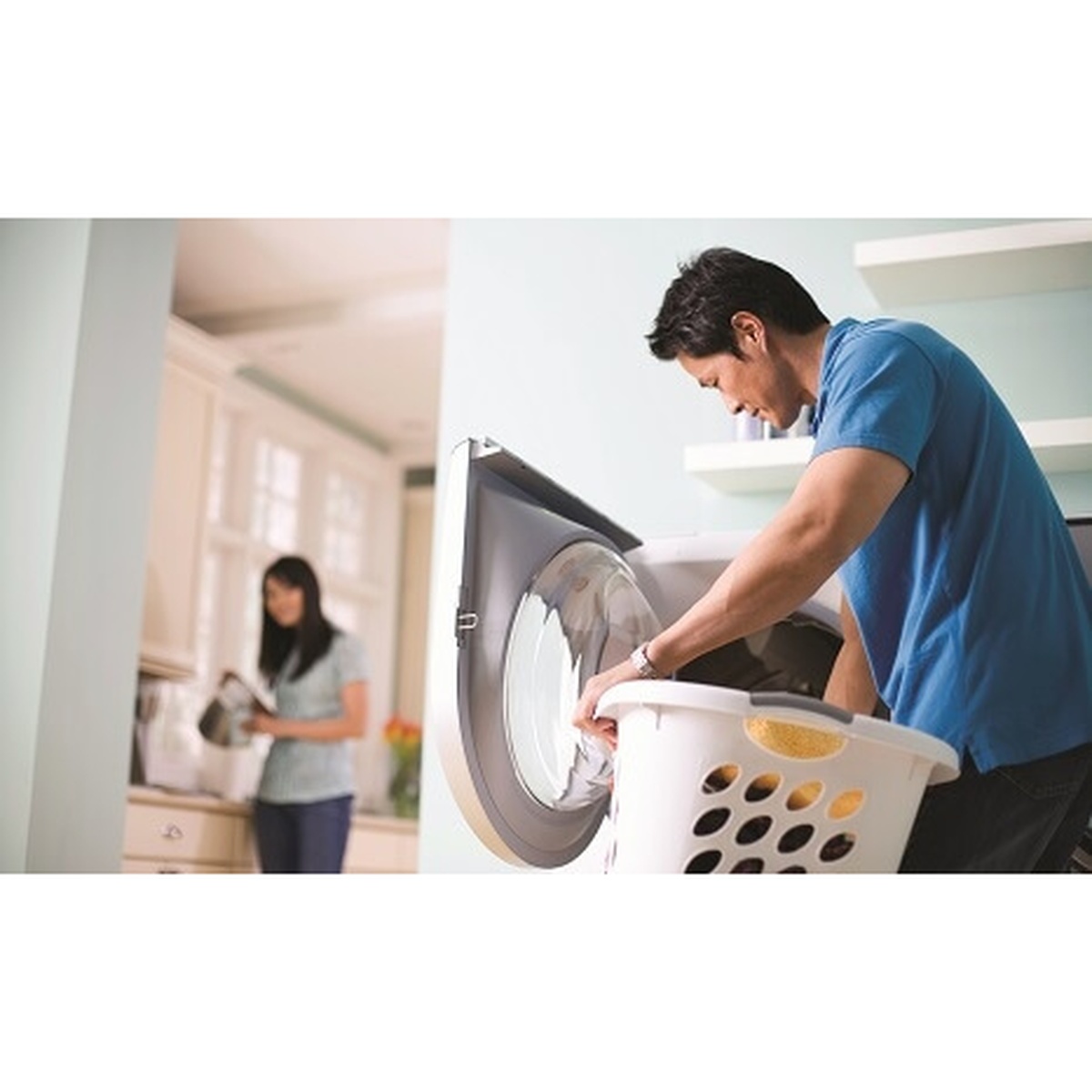 Man loading clothes into a front-load washer from a laundry basket in a home environment